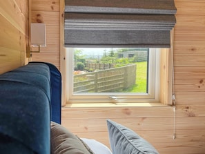 A cozy room with a wooden interior, a window with a view of a fenced garden, and a blue couch with pillows.