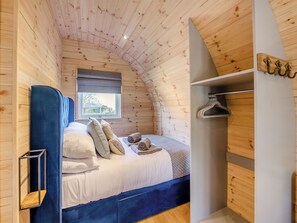 A cozy bedroom with a curved ceiling, a bed with white bedding, a blue headboard, and a window with a view of greenery.