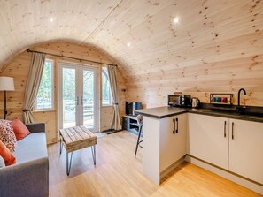 Interior acogedor de una cabaña con techo de madera, comedor, kitchenette y un ventanal con cortinas.