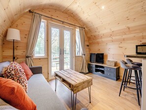 Interior acogedor de una cabaña con techo de madera, un sofá, una mesa, un televisor y una zona de bar.