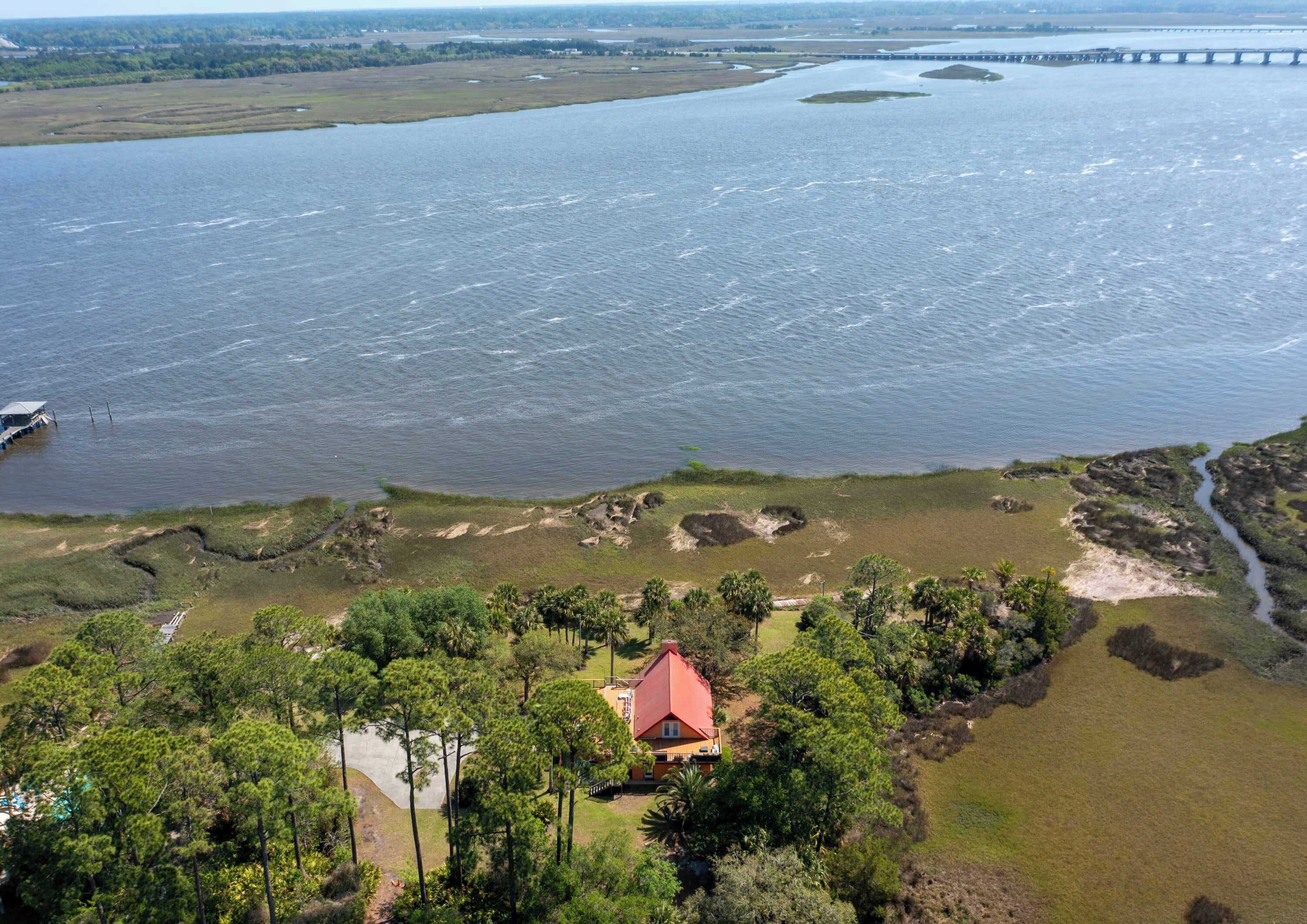 A coastal property with a red-roofed building, a dock, and a bridge in the background.