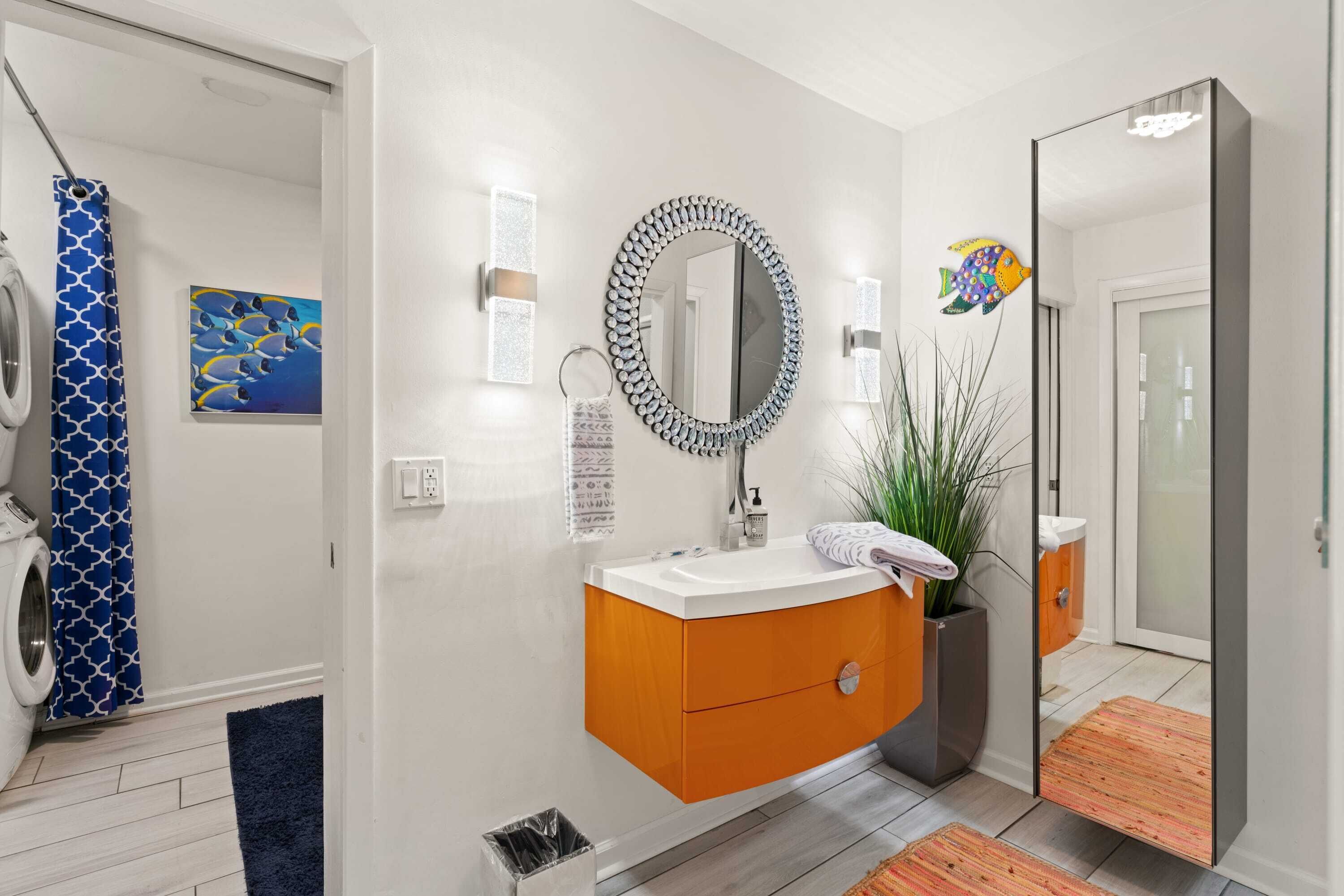 Un bagno moderno con un lavandino bianco, un mobile vanitario arancione, uno specchio grande e una tenda da doccia con un motivo blu.