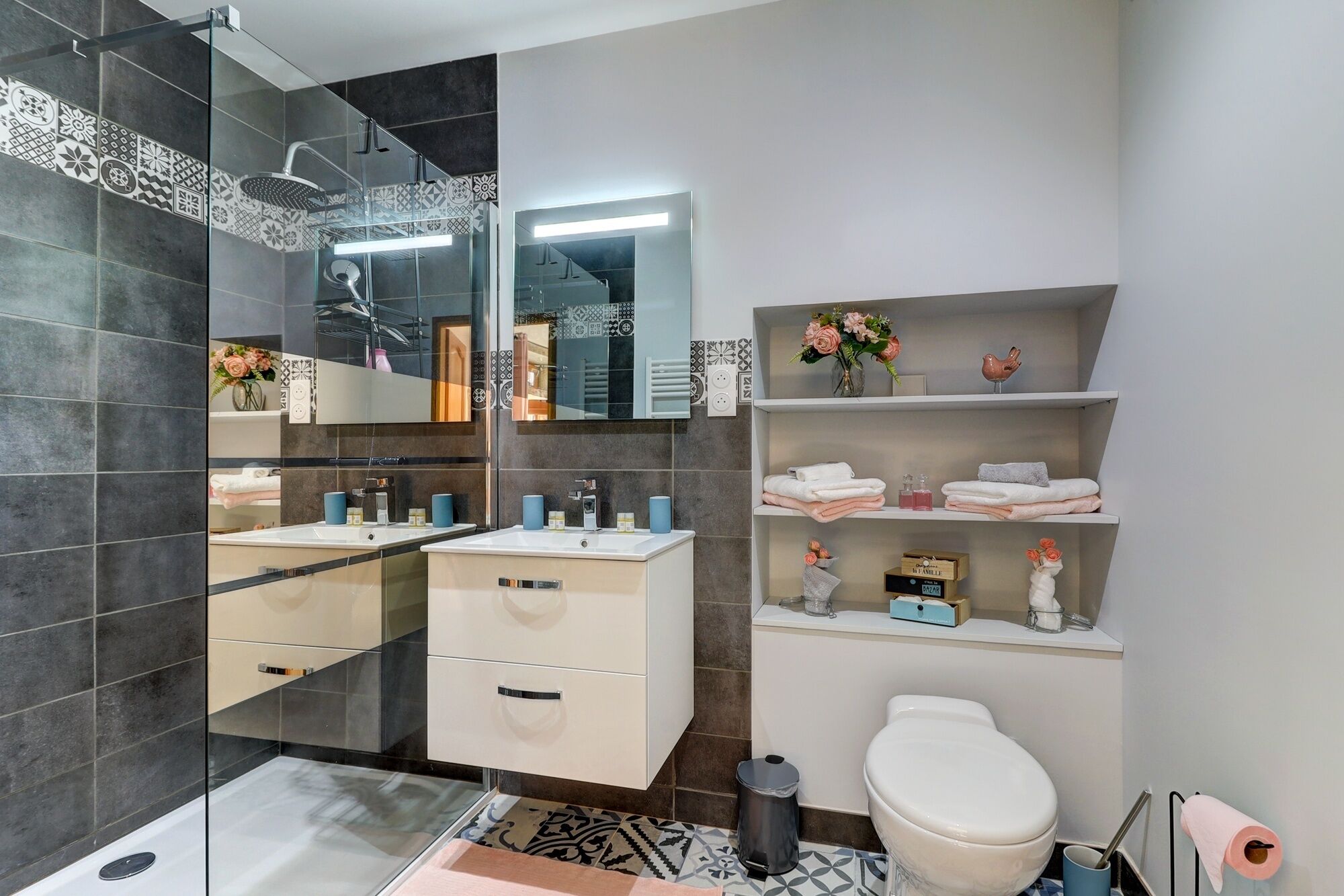 A modern bathroom with dark tiles, a glass shower enclosure, a white sink, and a toilet.