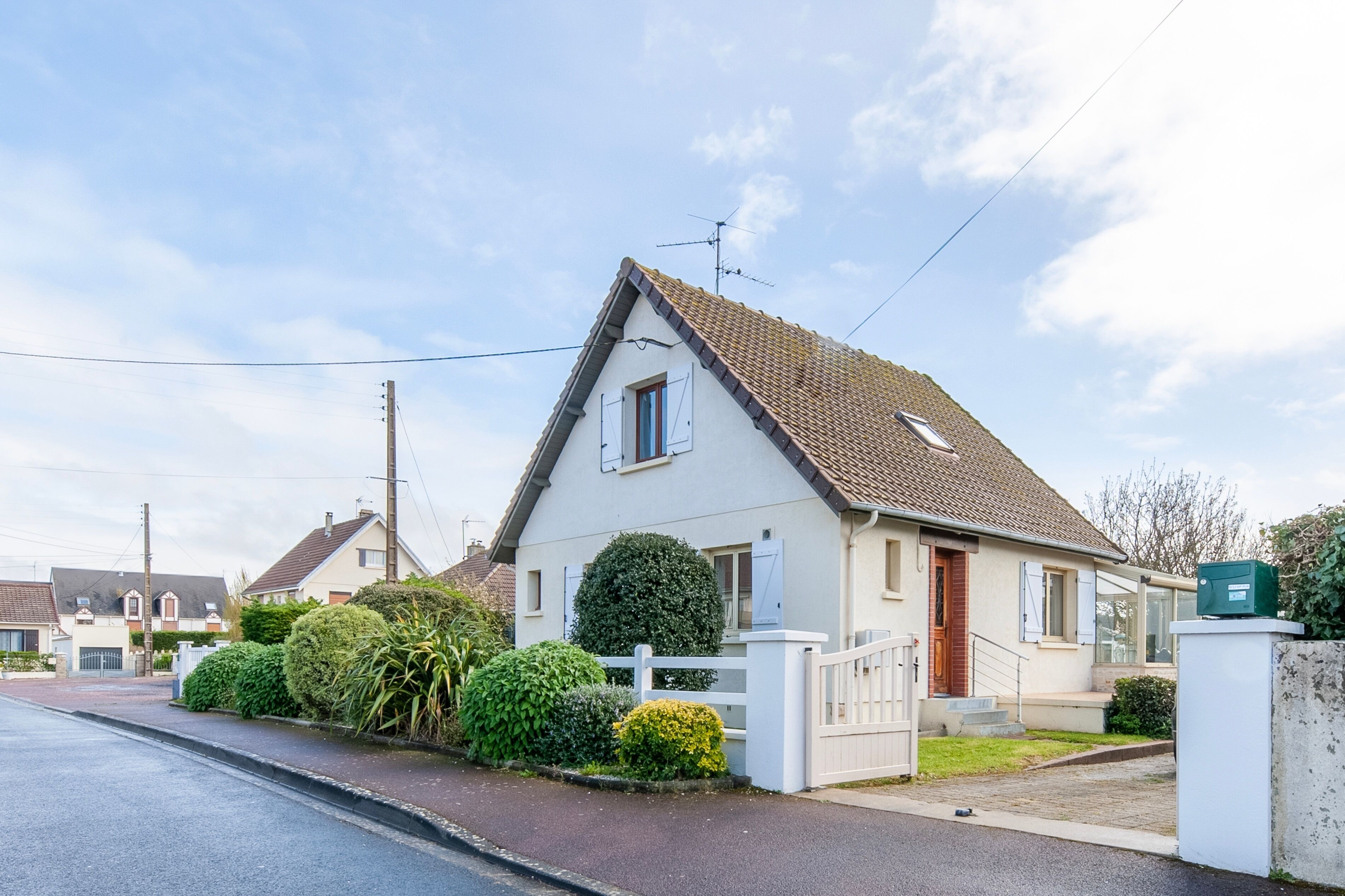 Ein eingeschossiges Haus mit einem Ziegeldach, einem weißen Zaun und einem kleinen Vorgarten mit Büschen.