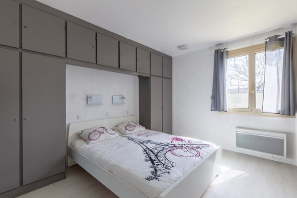 Une chambre à coucher avec un lit, une armoire grise et une fenêtre avec des rideaux.