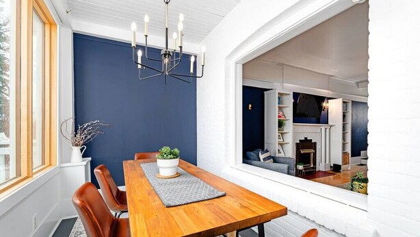 A dining area with a wooden table, brown chairs, a chandelier, and a view into a living room with a fireplace.