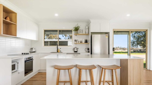 Una cocina moderna con una isla central, taburetes de madera, horno empotrado y vistas amplias a través de grandes ventanales.