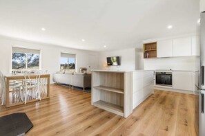 Une cuisine moderne avec des meubles blancs, un four encastré et un coin repas comprenant une table et des chaises en bois.