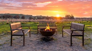 Vista del atardecer con tres bancos de madera y un pozo de fuego en un campo cubierto de hierba.