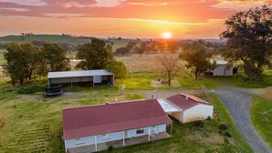 Une propriété rurale comprenant une grande maison, un petit abri et un espace clôturé avec un trampoline.