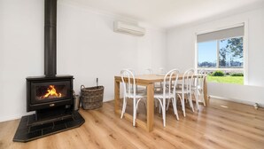 Una habitación con estufa de leña, una mesa de comedor con sillas, una ventana con vistas y un equipo de aire acondicionado.