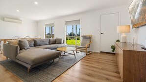 Una sala de estar moderna con un sofá seccional, una mesa de centro de madera, un sillón mecedora y vistas a un campo verde a través de amplias ventanas.