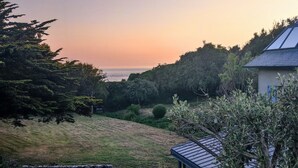 A house with a stone patio and outdoor seating area overlooking a grassy landscape and the sea.