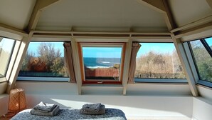 A room with a bed, a window with curtains, and a view of the sea.