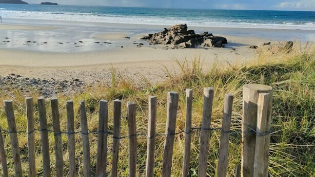 A beach with a wooden fence and a rocky outcrop in the distance.