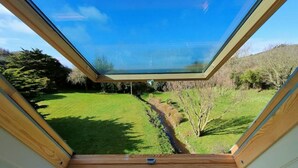 A room with a skylight, a view of a green landscape, and a small table with a device.