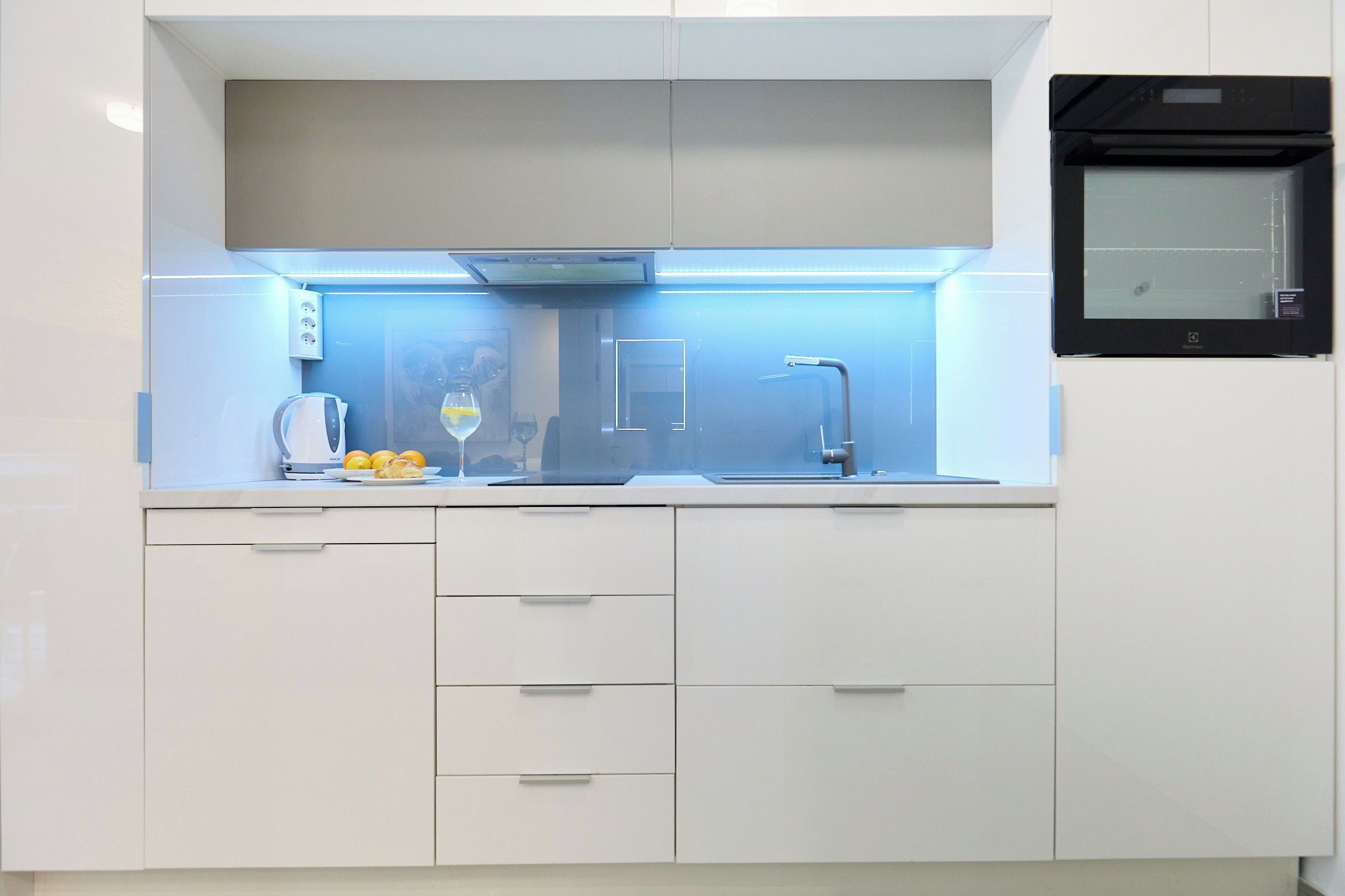 A modern kitchen with white cabinets, a stainless steel sink, and a built-in oven.