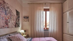 Une chambre à coucher avec un lit, une table de chevet, une fenêtre avec des rideaux et un radiateur.