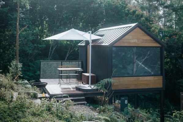 A modern, compact cabin with a wooden deck, a dining area, and a large window.