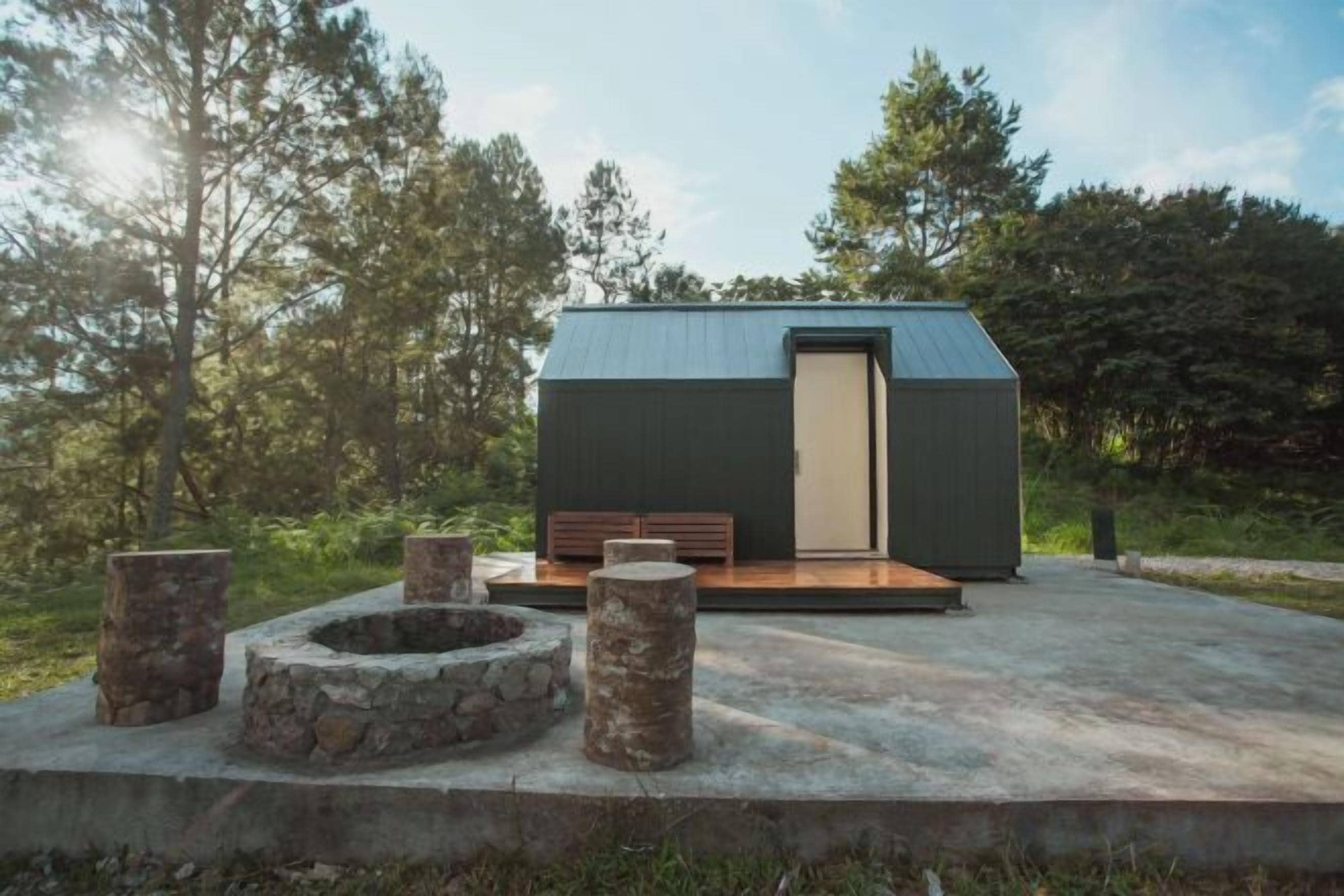 Een moderne cabin met een plat dak, een houten terras en een vuurplaats.