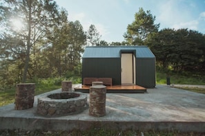 Une cabane moderne dotée d’un toit plat, d’une terrasse en bois et d’un espace aménagé pour faire un feu de camp.