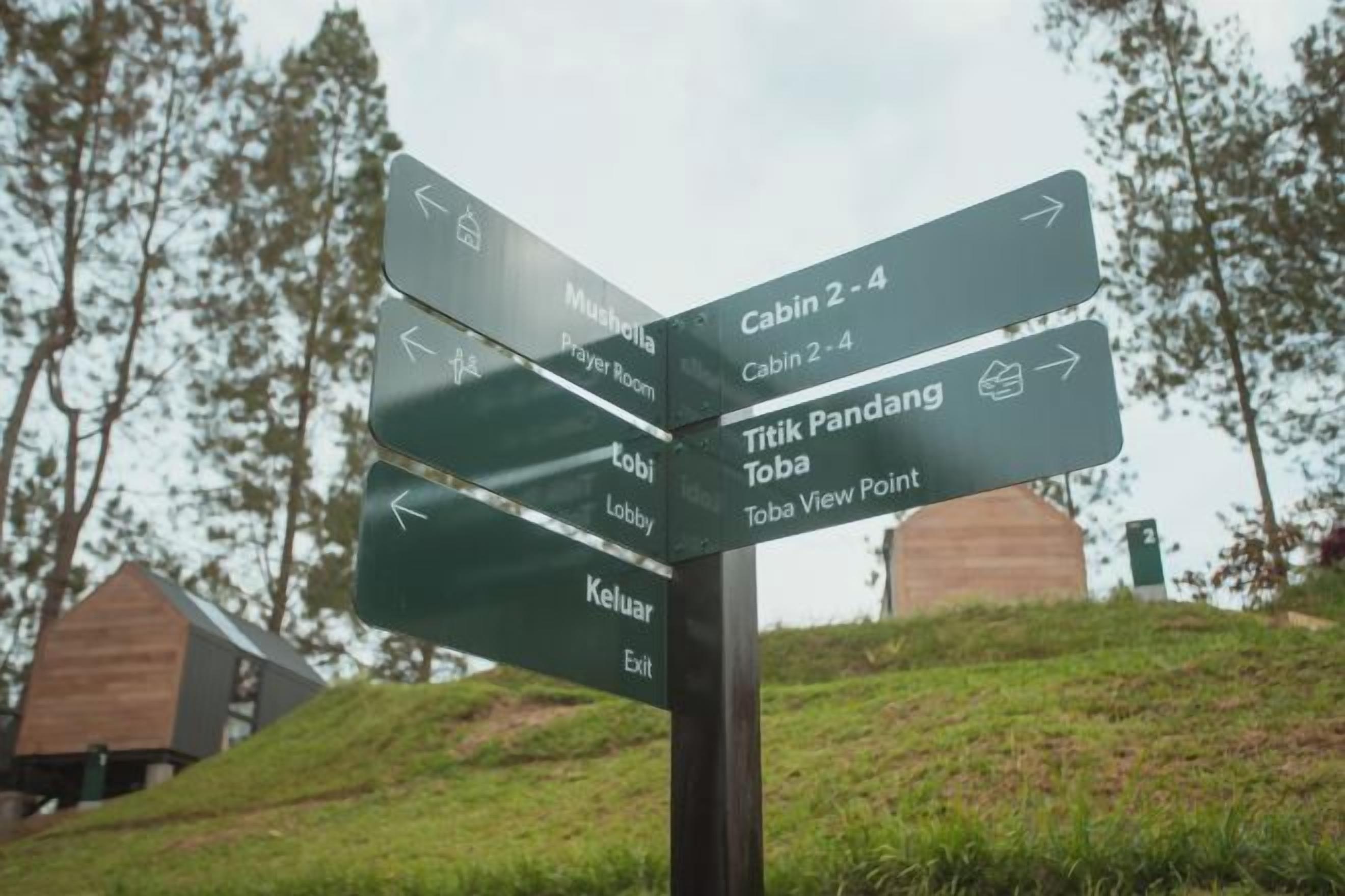 Un cartel direccional con varias flechas indicando diferentes lugares, como cabañas, la recepción y un mirador.