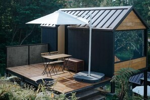 A small wooden structure with a sloped roof, a table and chairs, and a large umbrella.