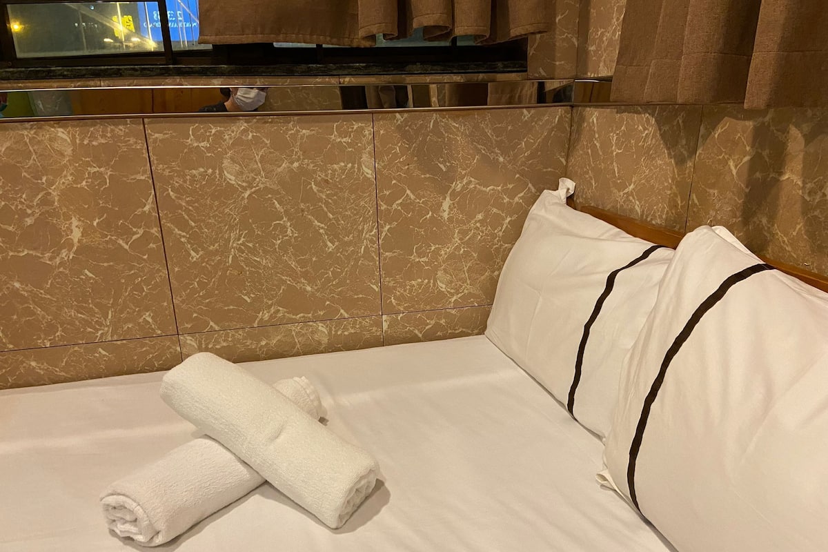 A hotel room with a bed, a folded towel, and a TV mounted on the wall.