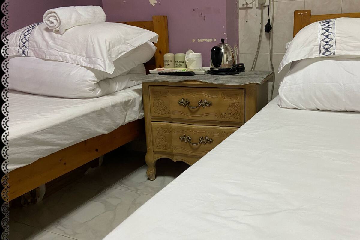 A bedroom with two single beds, a nightstand with a kettle, and a wall socket.