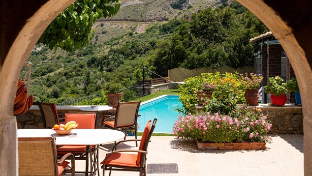 Une terrasse extérieure avec une piscine, entourée de chaises et d’une table, offrant une vue sur un paysage montagneux.
