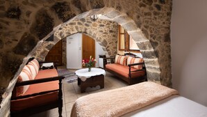 Une pièce chaleureuse avec une arche en pierre, un lit, deux canapés et une petite table sur laquelle est posé un vase de fleurs.