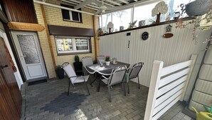 Eine Terrasse mit Tisch, Stühlen, einer Tür und einem Fenster.