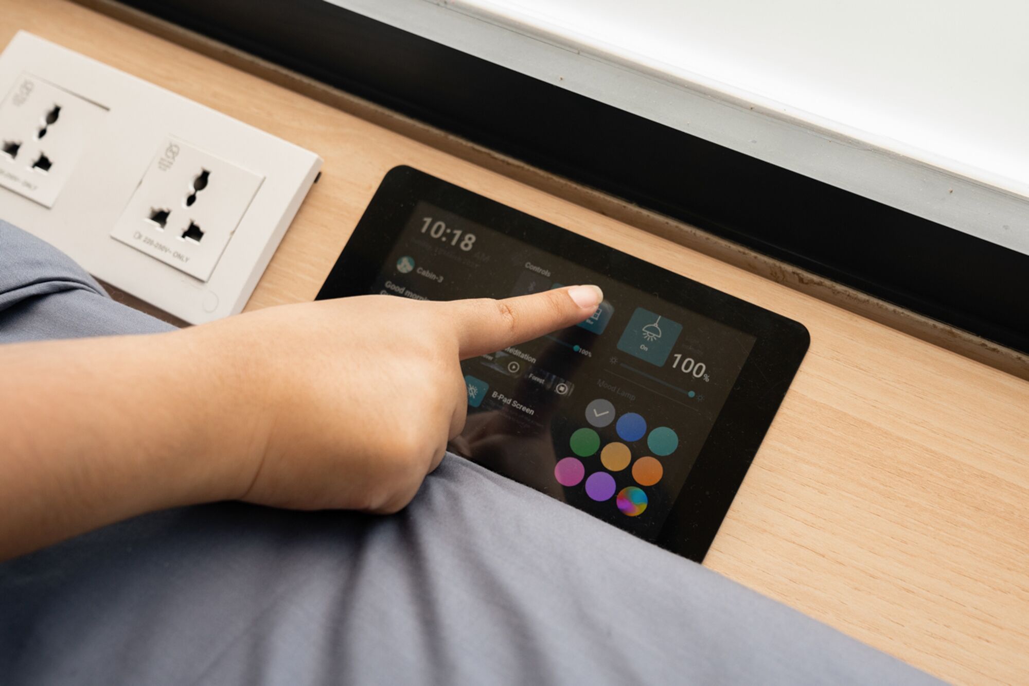 A person using a tablet on a bed with a visible power outlet and a window sill.