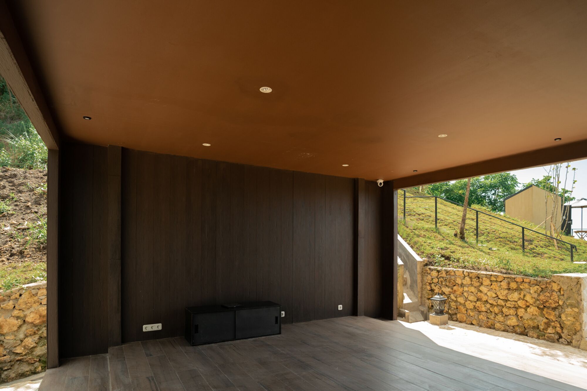 Un espace intérieur avec un mur en bois foncé, un meuble noir et un mur en pierre à l’extérieur.