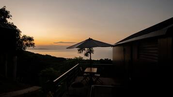 A deck with a table and chairs, overlooking a scenic view of hills and a sunset.