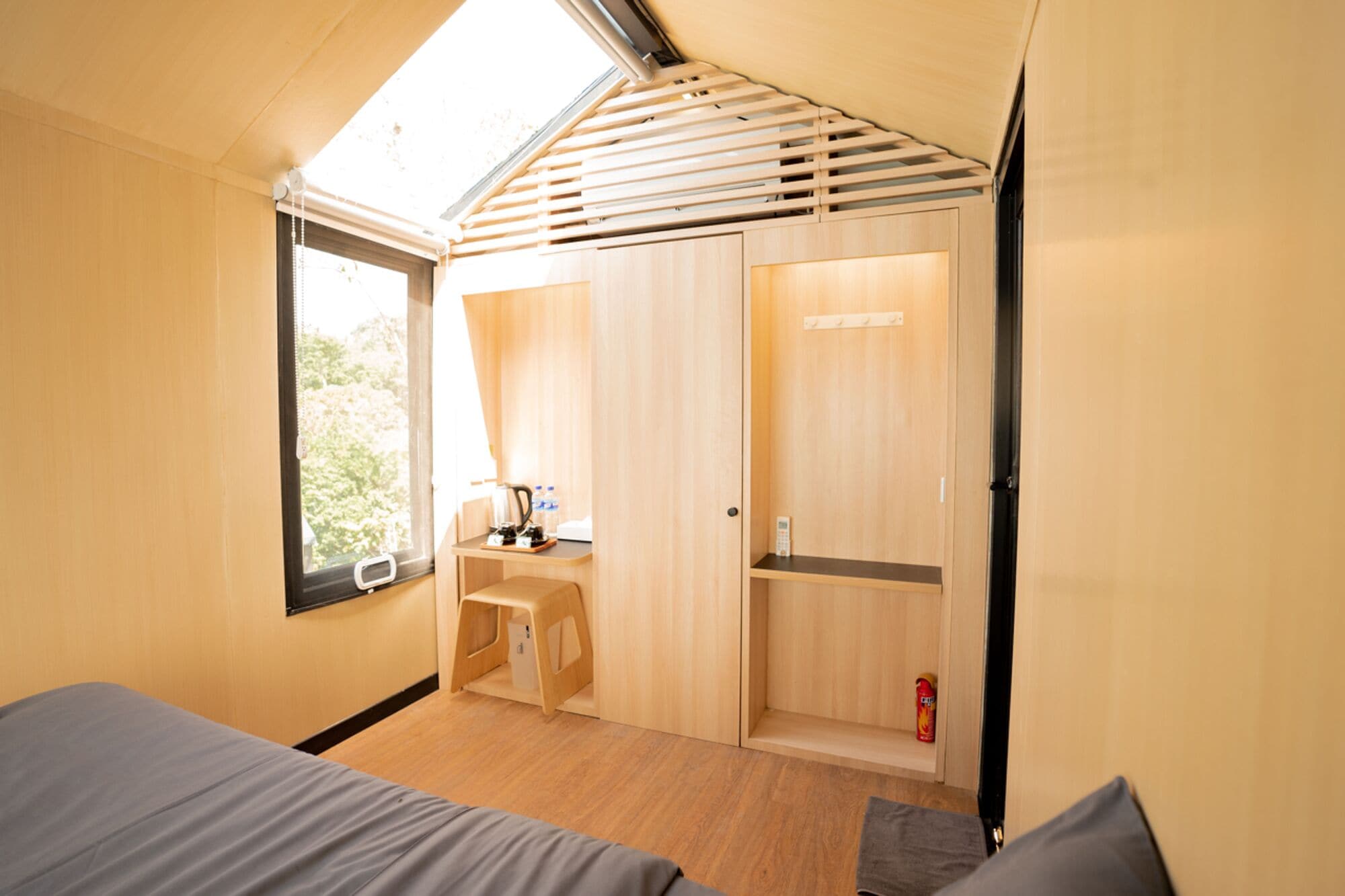 Ein kompakter, moderner Raum mit einem Bett, einem kleinen Tisch mit Wasserkocher und einem Kleiderschrank.