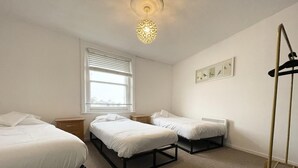 Une chambre avec deux lits simples, une fenêtre avec des stores, un luminaire au plafond et un radiateur fixé au mur.