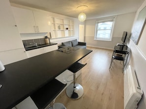 A modern kitchen with a central island, white cabinetry, and a dining area with a sofa.