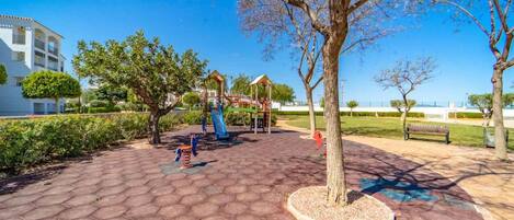 A playground with play structures, a paved area, and a bench.