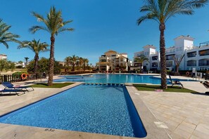 A swimming pool with lounge chairs, palm trees, and modern buildings in the background. - Beautiful apartment overlooking the pool- MO2411LT (La Torre Golf Resort)