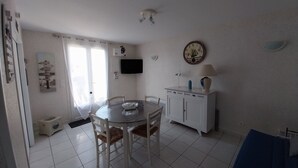 A dining area with a round table, chairs, a television, and a clock on the wall. - Charming apartment with WIFI 5 minutes walk from the beach and town center (Saint-Palais-sur-Mer)