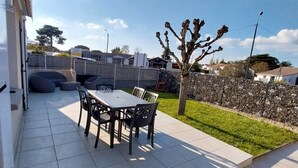 A patio area with a tiled floor, a table with chairs, a small tree, and a stone wall. - Charming apartment with WIFI 5 minutes walk from the beach and town center (Saint-Palais-sur-Mer)