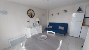 A compact living space with a round dining table, a blue sofa, a white cabinet, and a small refrigerator. - Charming apartment with WIFI 5 minutes walk from the beach and town center (Saint-Palais-sur-Mer)