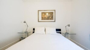 A hotel room with a large bed, two bedside tables with lamps, a framed artwork on the wall, and a plain white wall. - Beach House Oasis - 2BR Apartment with backyard patio in the Beaches Area (Toronto)