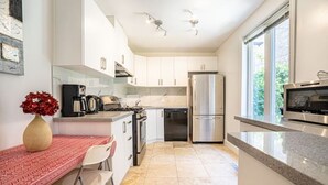 A modern kitchen with white cabinets, stainless steel appliances, and a red patterned tablecloth. - Beach House Oasis - 2BR Apartment with backyard patio in the Beaches Area (Toronto)