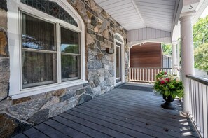 A stone house with a wooden porch, large windows, and a potted plant.