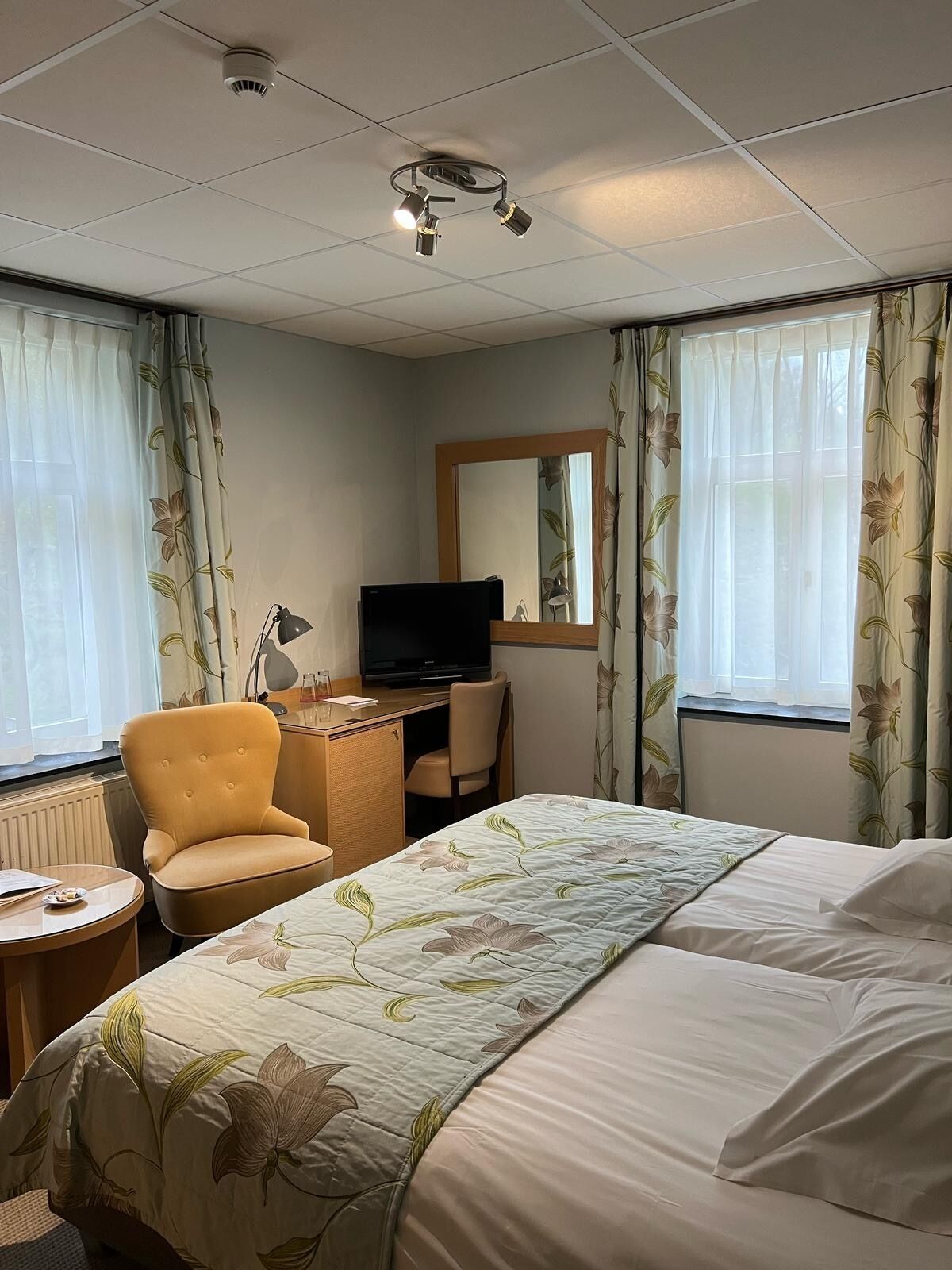 Een hotelkamer met een bed, een bureau met een televisie, een stoel en een klein tafeltje.