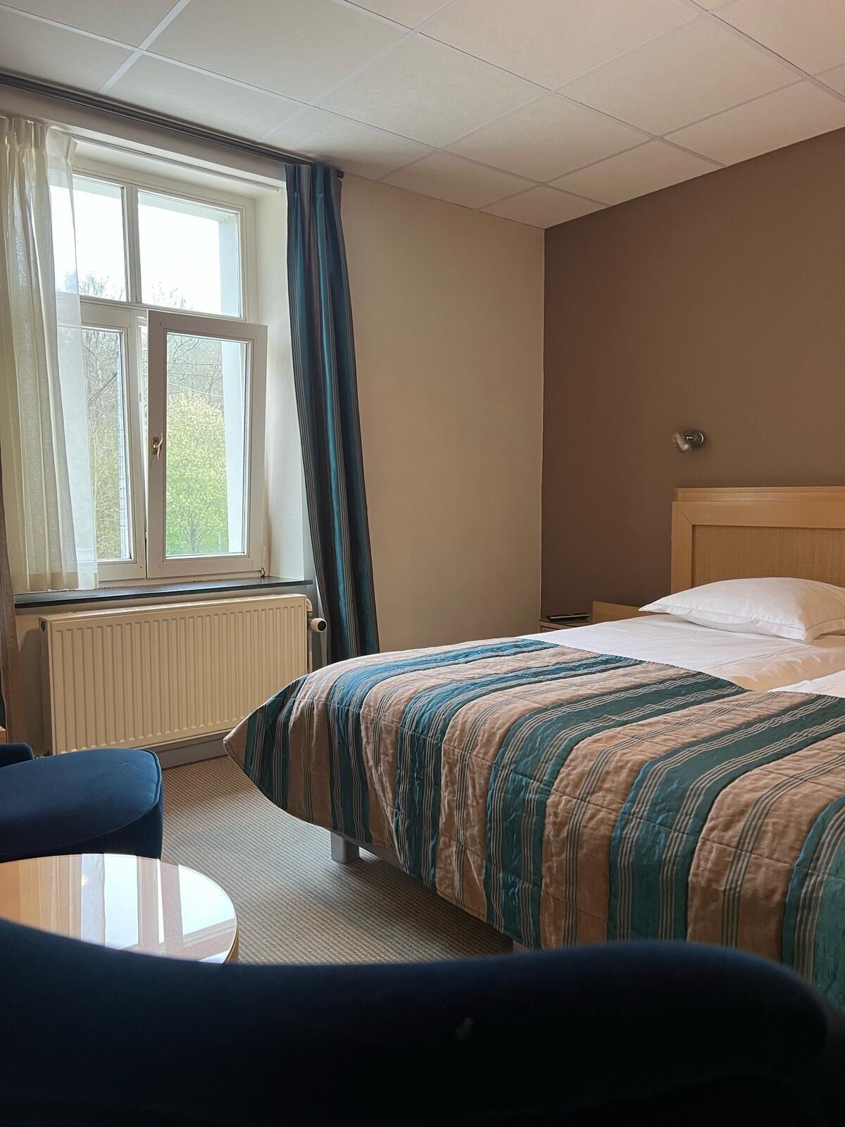 Ett hotellrum med en säng, ett runt bord och ett fönster med gardiner.