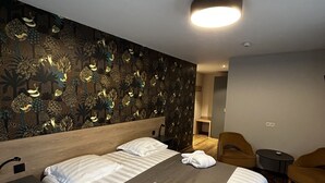 A hotel room with a large bed, two white pillows, a grey blanket, and a wooden headboard. There are two white towels on the bed and a small table with a lamp. - Moulin de Daverdisse (Daverdisse)