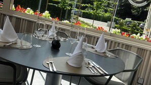 A dining table set with white napkins, cutlery, and wine glasses, overlooking a garden with flowers and trees. - Moulin de Daverdisse (Daverdisse)